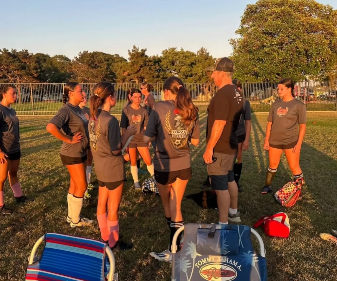 A coach talking a group of players through a drill in late afternoon light